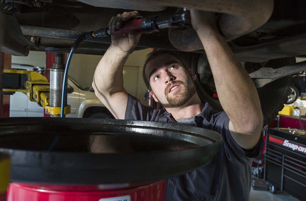 Vehicle service technician draining oil from car.