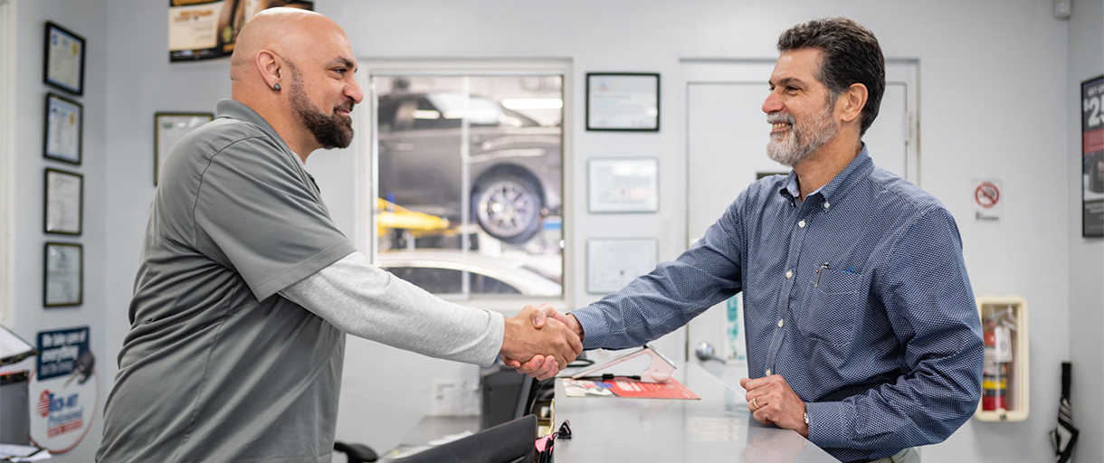 Image of two men shaking hands across a counter in an automotive service center.