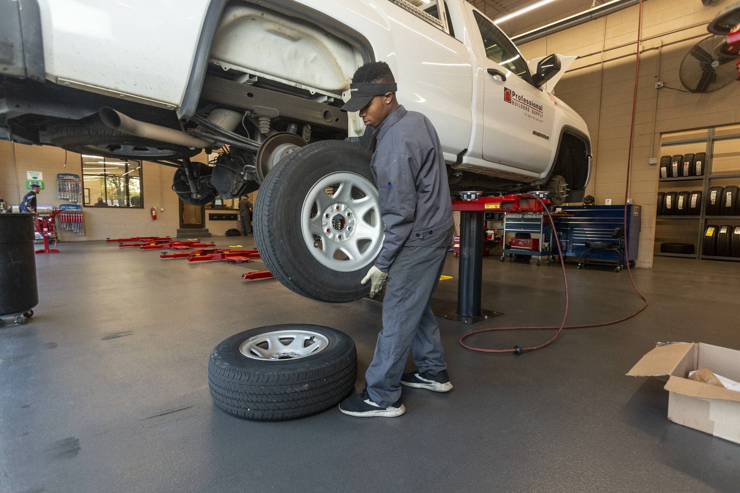 Car technician changing a tire on a white pickup truck.