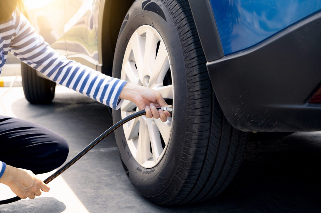 A person kneels next to a car tire, using an air hose to check or inflate the tire.