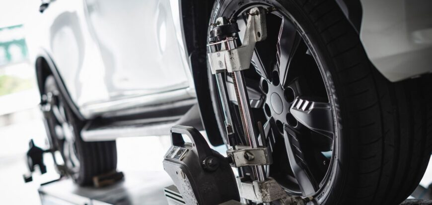 Car undergoing wheel alignment with a measurement device attached to the front tire, ensuring proper balance and alignment.