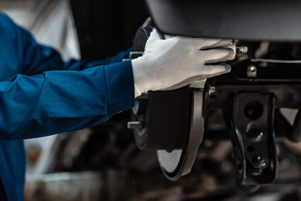 A mechanic wearing white gloves and a blue uniform is repairing a car's brake disc, focusing on the brake assembly.