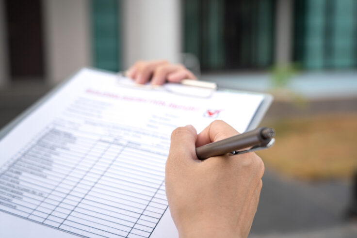 A close-up of a person filling out a car inspection checklist on a clipboard, with a blurred outdoor background.